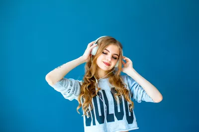 jovem mulher loira usando headphone branco fundo azul