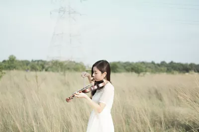 menina vestida de branco tocando violino pasto